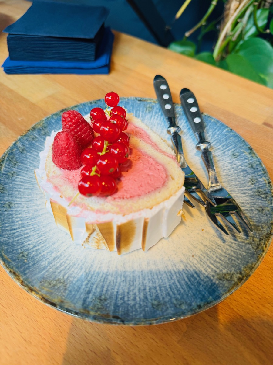 Slice of sponge roll with raspberry cream, raspberries and redcurrants on a blue plate