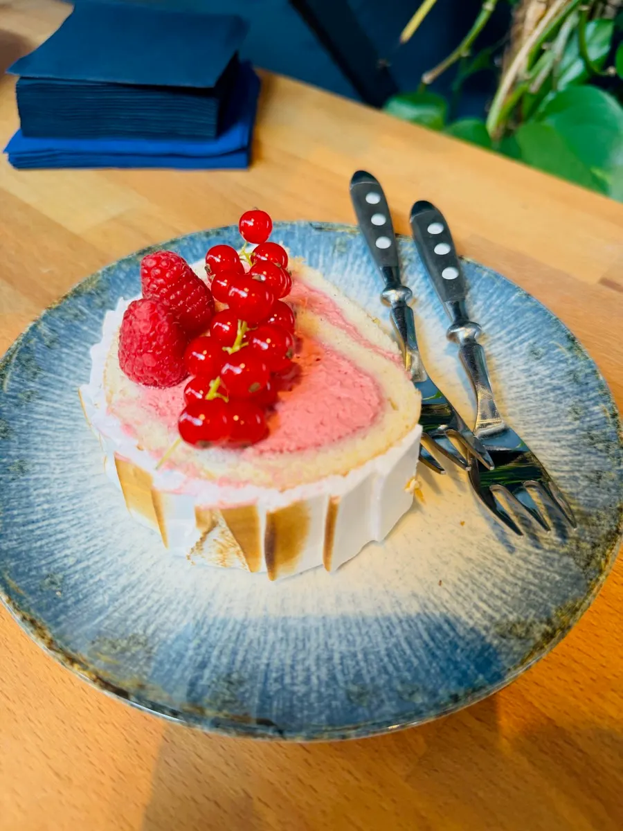 Stück Biskuitrolle mit Himbeercreme, Himbeeren und roten Johannisbeeren auf blauem Teller