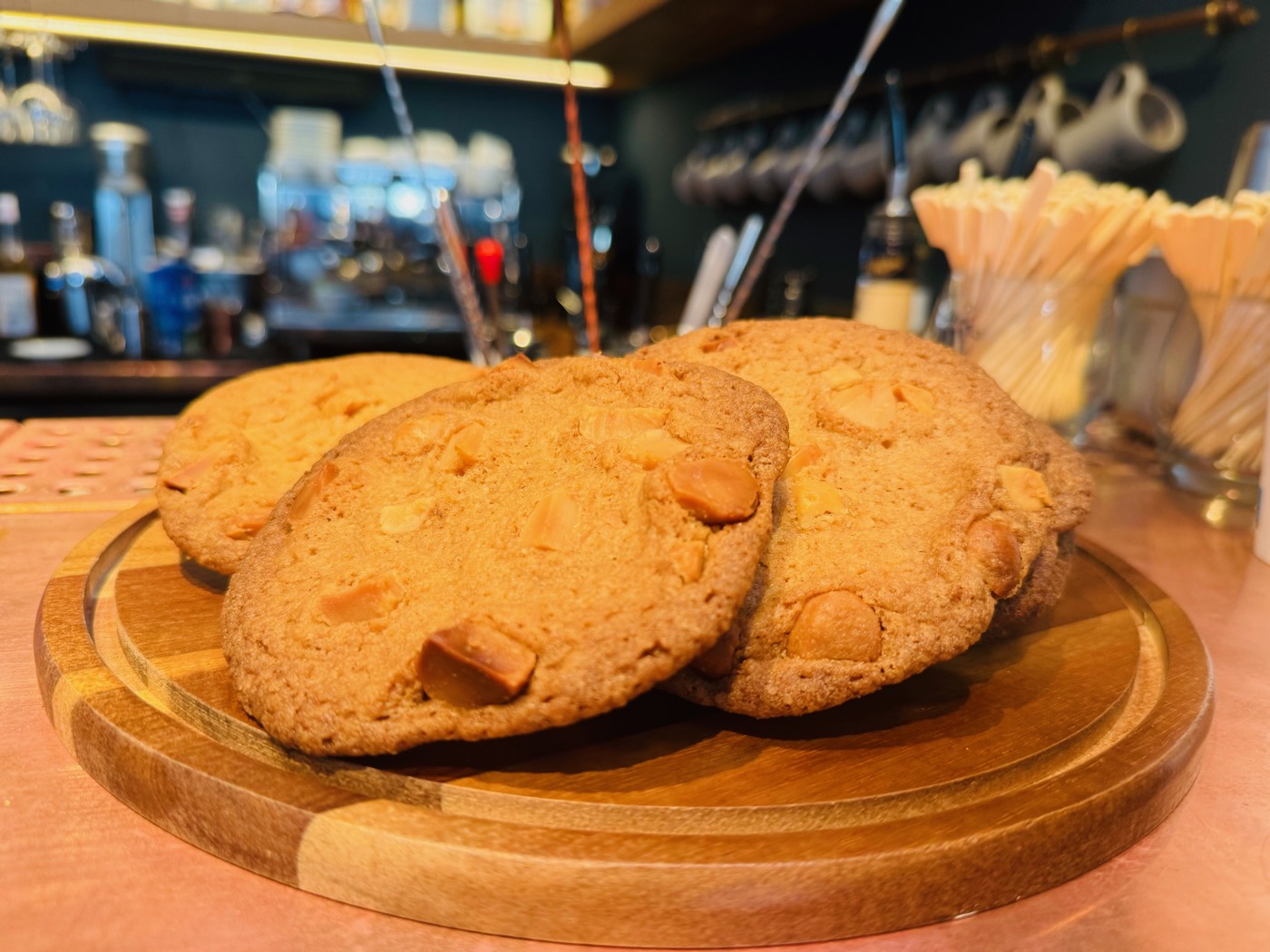 Three large cookies with nuts on a wooden board in front of the bar