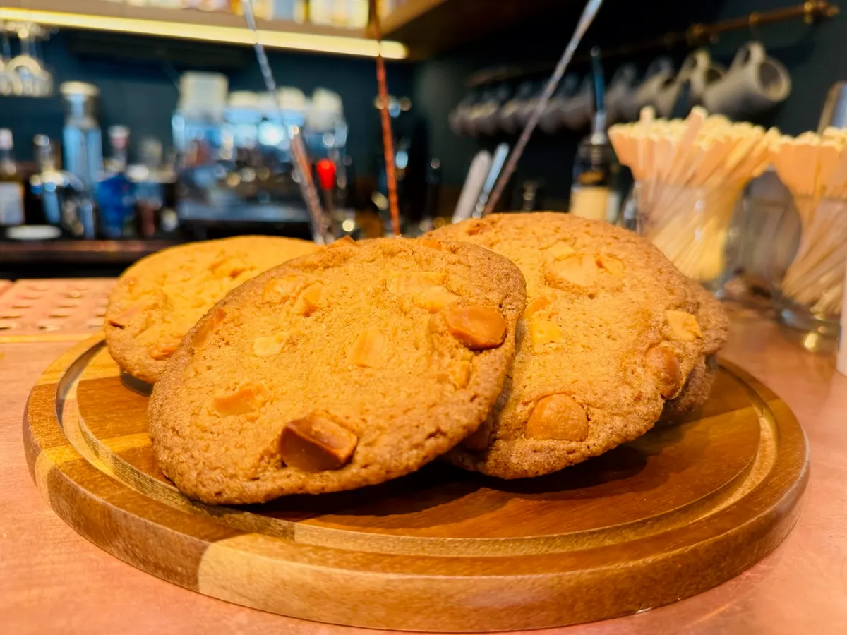 Drei große Cookies mit Nüssen auf einem Holzbrett vor der Bar