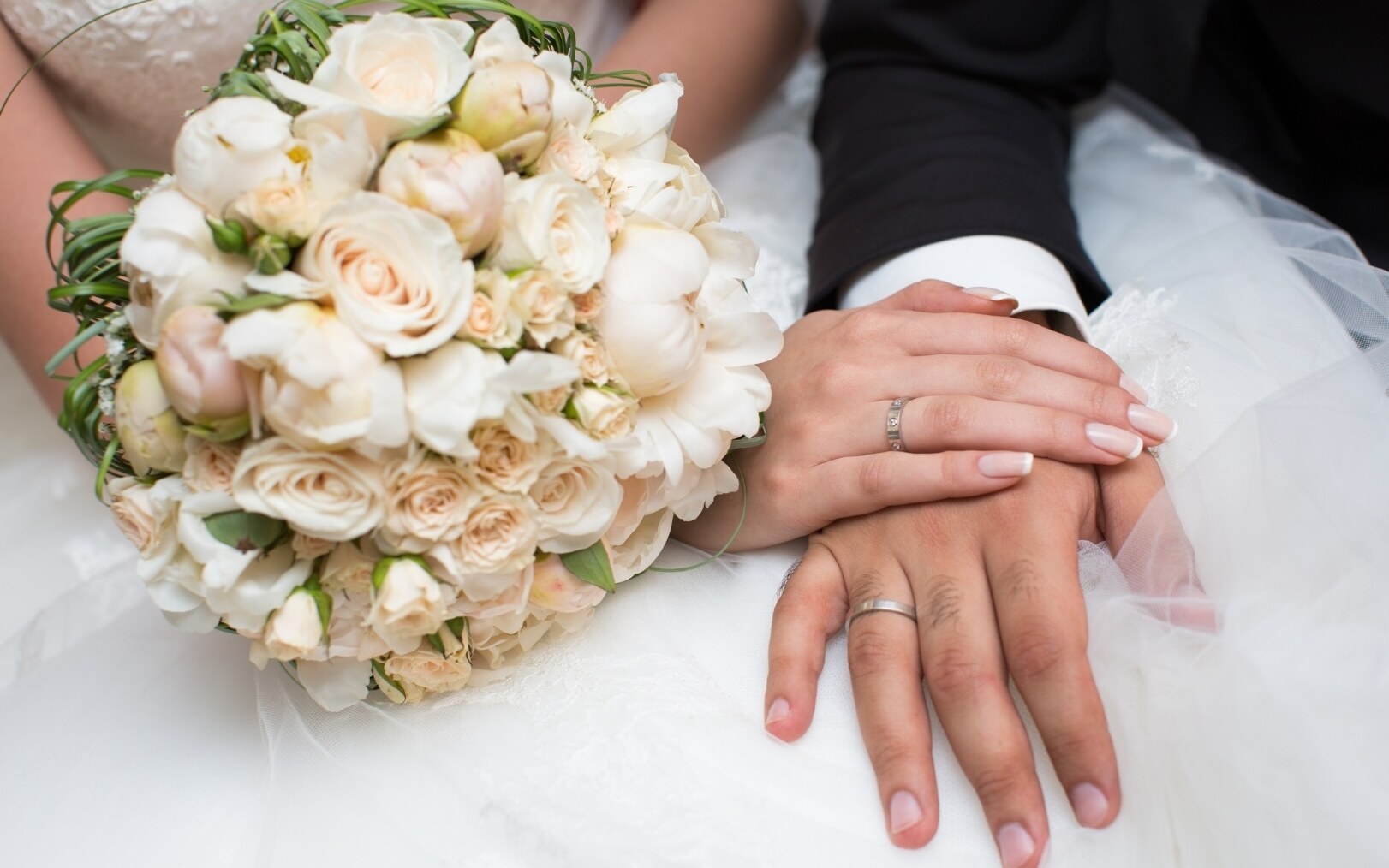 Bridal bouquet and the couple's hands with wedding rings at the THE DUKE distillery